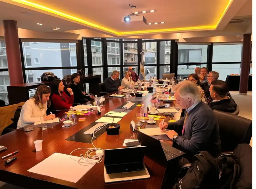 Reunión de trabajo alrededor de una mesa larga con cuadernos y computadoras.